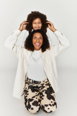 Bir anne ve kızı, gri bir zemine karşı şık hayvan desenli kıyafetlerle kahkahalarını paylaşıyor..