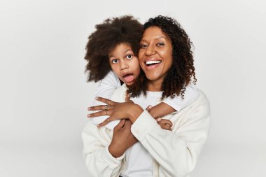 Bir anne ve kız neşe içinde birlikte poz veriyorlar. Şık kıyafetler içinde, sevgi ve tarz gösteriyorlar..