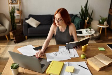 Genç ve güzel bir kadın, çizimler ve dizüstü bilgisayarla çevrili yaratıcı görevlerine odaklanıyor..