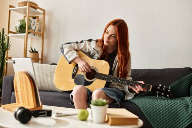 Güzel kızıl saçlı genç bir kadın rahat bir kanepede otururken gitar çalmaktan hoşlanır..