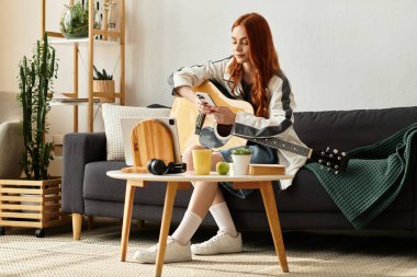 Genç bir kadın kanepede dinleniyor, gitar çalıyor ve rahat bir odada akıllı telefonunu kullanıyor..