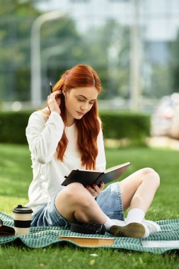 Genç bir kadın piknik battaniyesinde oturuyor, çevresinden zevk alıyor ve yazıyor..