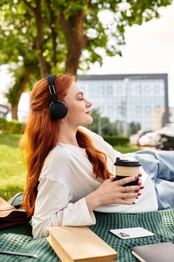 Genç bir kadın boş zamanlarını müzik dinleyerek ve parkta kahve içerek geçirir..