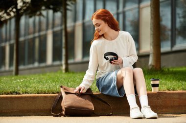 Genç ve güzel bir kadın çimenlerde dinleniyor, kahvesini yudumluyor ve müziğinin tadını çıkarıyor..