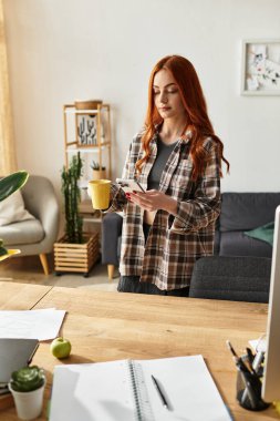 Güzel, genç bir kadın, parlak, şık bir yaşam alanında telefonunu kullanırken kahvesini yudumluyor..