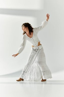 Genç bir kadın, parlak bir mekanda, dalgalı beyaz bir elbiseyle zarif bir şekilde dans eder..