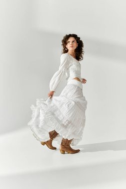 Güzel, genç bir kadın zarif bir şekilde beyaz bir elbise ve botla yürüyor, şık görünümünü sergiliyor..