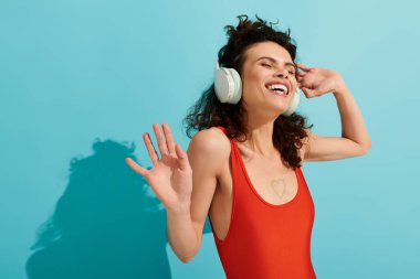 Genç ve güzel bir kadın, parlak mavi bir arka planda neşeyle dans ederken müzikten zevk alır..