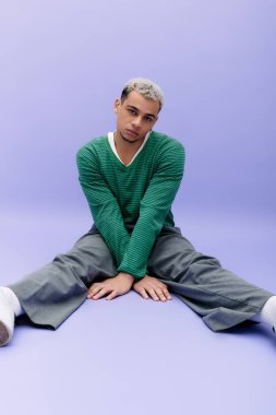 Genç bir Afro-Amerikan erkeği dikkat çekici mor bir arka planda kendine güvenen bir şekilde poz veriyor..