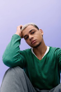 Genç bir Afro-Amerikan erkeği şık kıyafetlerini ve boyalı saçlarını gösterirken kendine güvenerek poz verir..