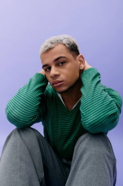 Saçları boyalı, şık bir genç adam mor bir arka planda kendine güvenerek poz veriyor..