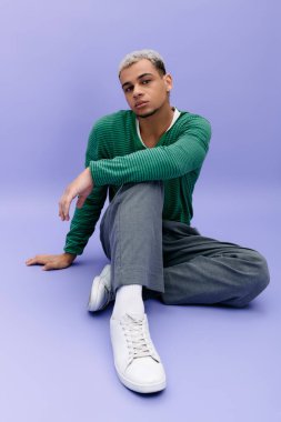 Saçları boyalı genç bir siyah adam, mor bir arka plana karşı, modaya uygun bir şekilde poz veriyor..