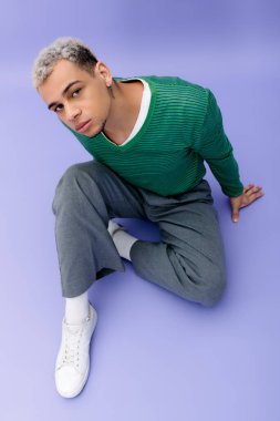 Şık, genç, siyah bir adam canlı, mor bir arka plana karşı duruyor..