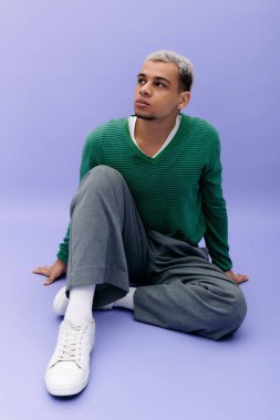 Boyalı saçlı genç bir adam canlı mor bir arka plana şık bir şekilde poz verir..