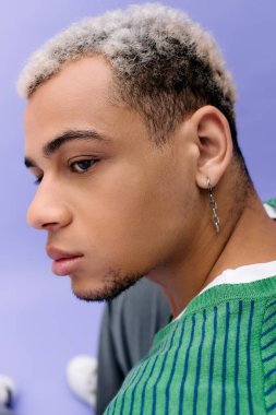 Saçları boyalı, kendine güvenen genç bir adam mor bir arka planda şık bir şekilde poz veriyor..