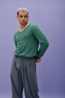 Saçları boyalı şık bir genç adam mor bir arka planda kendine güvenen bir şekilde poz verir..