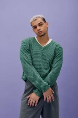 Genç bir Afro-Amerikalı adam kendine güvenerek şık bir elbise ve boyalı saçlarla poz veriyor..