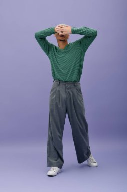 Kendine güvenen genç bir adam şık elbisesini canlı mor bir arkaplanda sergiliyor..