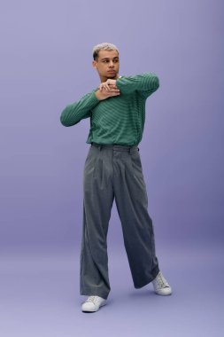 Genç bir Afro-Amerikalı, mor ayarı boyalı saçları olan şık bir kıyafet sergiliyor..