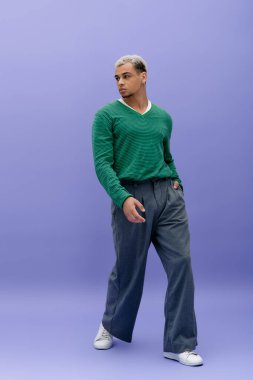 Tarz sahibi genç Afrikalı Amerikalı adam renkli bir arka planda kendine güvenen bir şekilde poz veriyor..