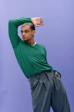 Şık giyinmiş genç siyahi bir adam mor bir arkaplana karşı güvenle poz verir..