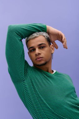 Genç Afrikalı Amerikalı erkek mor bir arka planda güven içinde poz verirken şık kıyafetler sergiliyor..