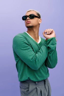 Kendine güvenen genç bir adam dikkat çekici mor bir arka planda saçları boyalı modaya uygun bir kıyafet sergiliyor..