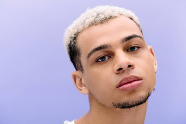 Saçları boyalı şık bir siyah adam mor bir fonda poz veriyor..