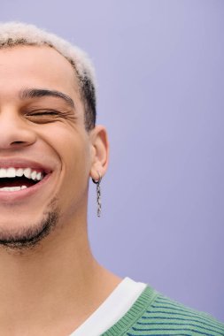 Saçları boyalı, Afro-Amerikalı genç bir adam şık bir kıyafetle poz verirken neşeyle gülümsüyor..