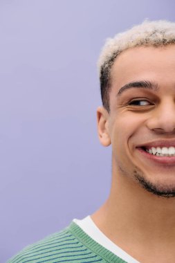 Renkli saçlı şık bir genç adam canlı mor bir arka planda poz veriyor..