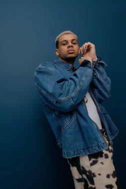 Genç bir Afro-Amerikan erkeği, kendine güvenen, boyalı saçlı, şık bir kot ceketle poz veriyor..