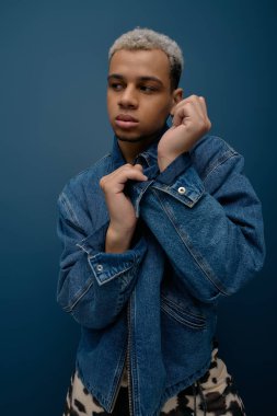 Genç bir Afrikalı Amerikalı zengin mavi bir arkaplana karşı çarpıcı bir kot elbise sergiliyor..