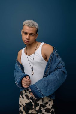 Genç bir Afro-Amerikan erkeği, modaya uygun bir kot ceketle modern tarzda poz veriyor..