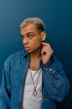 Kot ceketli genç siyah bir adam mavi bir arkaplanda gelişigüzel poz veriyor..