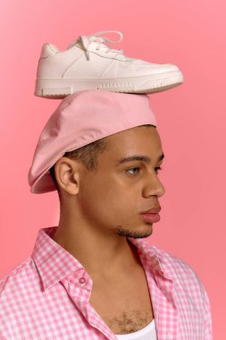 Genç siyahi bir adam canlı pembe bir arka plana karşı güvenle poz veriyor, tarzını sergiliyor..
