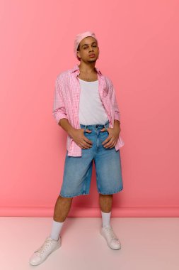 Kendine güvenen genç bir siyahi, canlı pembe bir arka plana karşı duruyor ve tarzını gösteriyor..