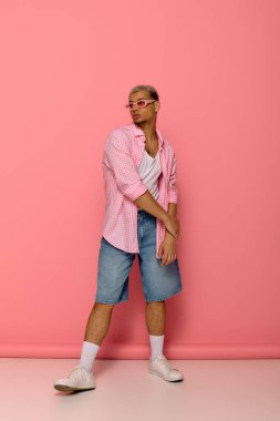 Şık genç adam kendine güvenerek poz veriyor, eşsiz moda anlayışını ve canlı saçlarını vurguluyor..