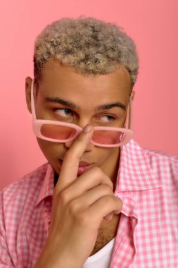 Saçları boyalı, genç, modaya uygun bir adam kareli gömlek ve pembe gözlüklerle poz veriyor..