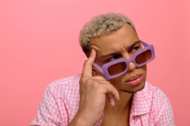 Genç bir Afro-Amerikalı, pembe arka planı olan kareli bir gömlekle güvenle poz veriyor..