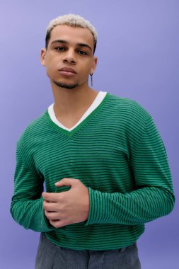 Saçları boyalı, kendine güveni tam bir genç adam canlı mor bir arka plana karşı şık bir kıyafet giyiyor..