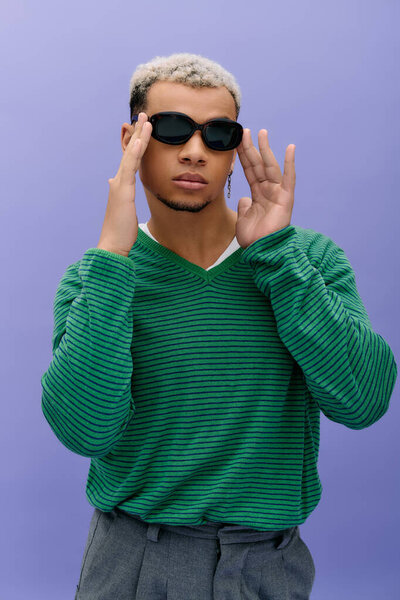 A young Black man poses in a stylish outfit against a purple background.