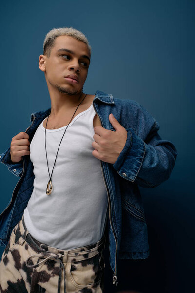 A confident young Black man styles a trendy denim jacket against a vibrant blue backdrop.