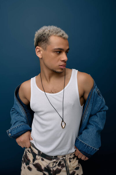 A young Black man with dyed hair shows his style in a denim jacket while posing.