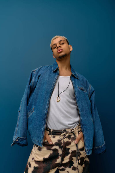 A young African American man showcases vibrant style with a denim jacket against a blue backdrop.