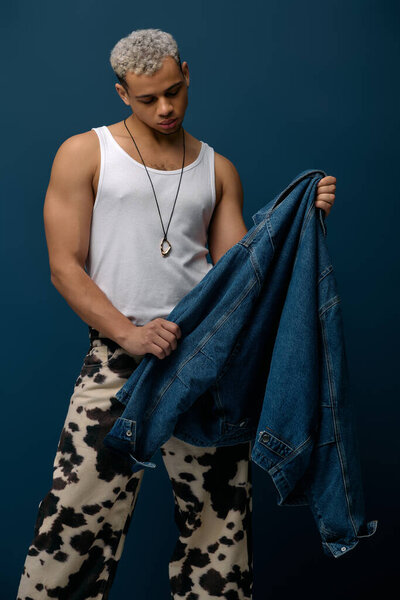 A stylish young African American man poses in a denim jacket on a striking blue background.