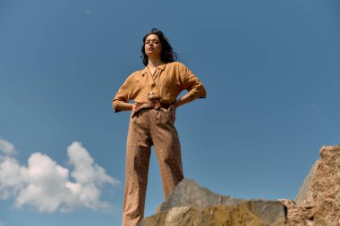 Kıvırcık saçlı genç bir kadın, modaya uygun yaz kıyafetlerini sergileyerek güvenli bir şekilde dışarıda poz veriyor..