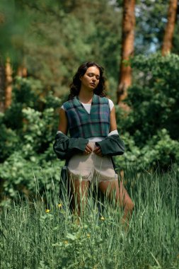 Genç bir kadın, ılık bir yaz gününde yemyeşil bir yağmurlukla şık bir şekilde poz verir..