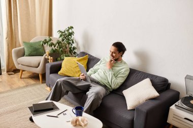 Genç yakışıklı bir adam rahat bir şekilde evinde uzanıyor, rahat bir gülümsemeyle dizüstü bilgisayarına odaklanıyor..