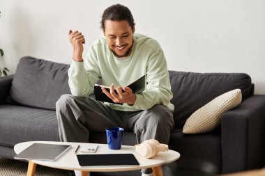 Genç yakışıklı bir adam kanepede rahatlar, bir kitapla meşgul olur ve içkisinin tadını çıkarır..