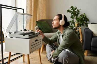 Genç bir adam, rahat bir evde pikabın yanında kulaklıkla müzik dinlemekten hoşlanır..